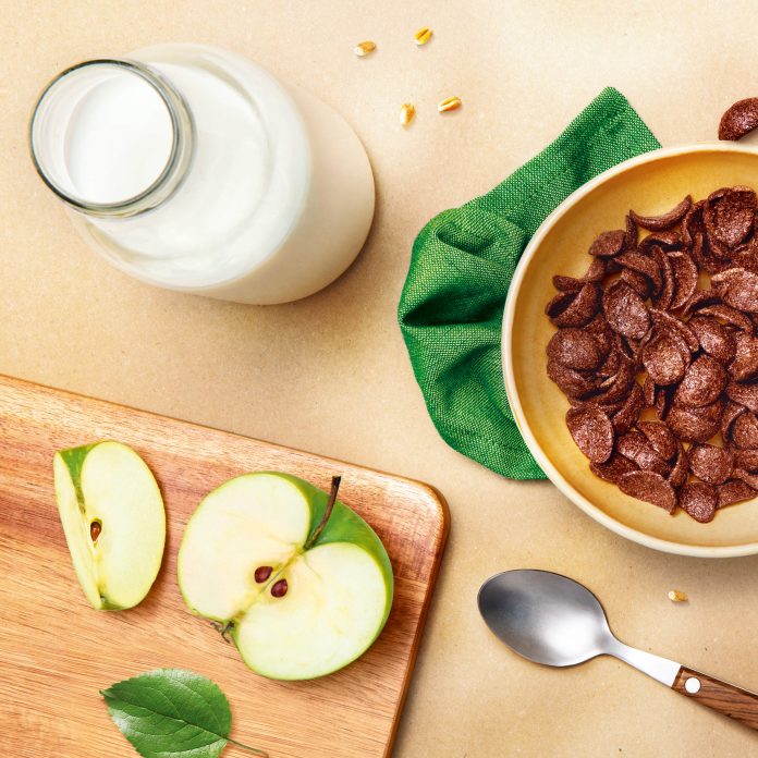 Top view image of Chocapic cereals with milk and apple in the background.