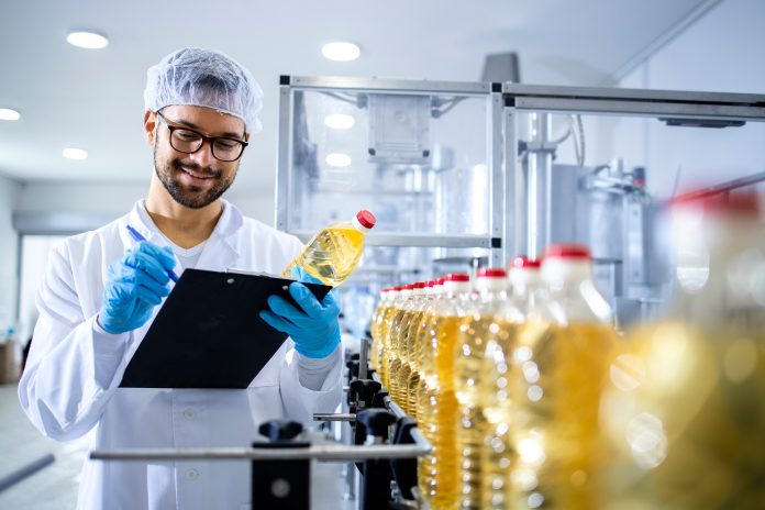 Food factory worker inspecting product quality and controlling production of refined edible bottled oil.